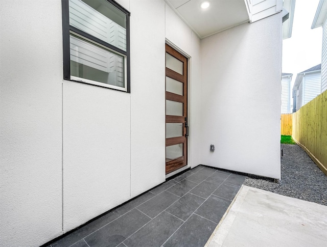 view of exterior entry featuring stucco siding, a patio area, and fence