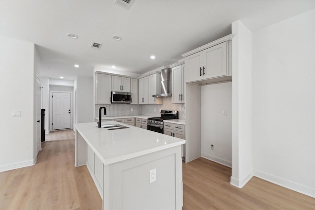 5013 Golden Forest Dr, Houston, TX 77091 - kitchen with appliances with stainless steel finishes, a sink, wall chimney range hood, light wood-style floors, and an island with sink