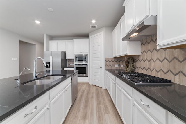 kitchen with appliances with stainless steel finishes, a sink, light wood finished floors, under cabinet range hood, and white cabinetry