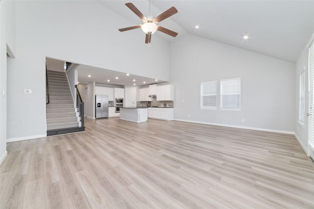 unfurnished living room with a ceiling fan, stairs, high vaulted ceiling, light wood-style floors, and recessed lighting