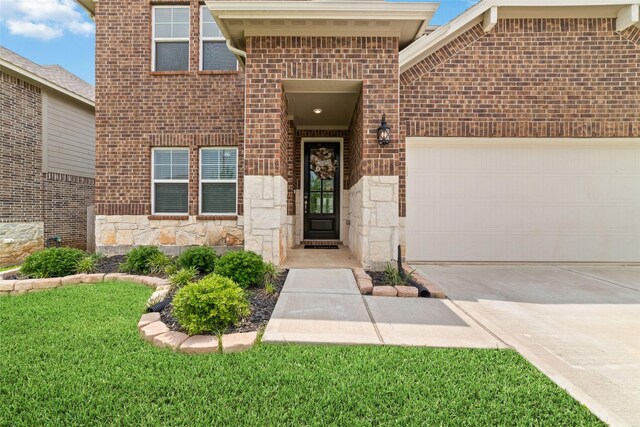 view of exterior entry featuring brick siding, a garage, driveway, and stone siding