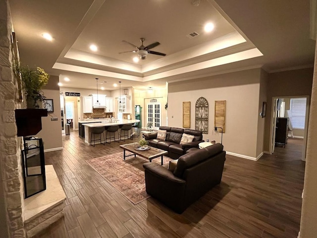 living room with visible vents, baseboards, dark wood-type flooring, a tray ceiling, and a ceiling fan