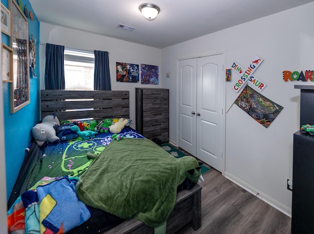 bedroom featuring baseboards, a closet, wood finished floors, and visible vents