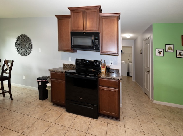kitchen featuring light tile patterned flooring, baseboards, washer and clothes dryer, dark stone countertops, and black appliances