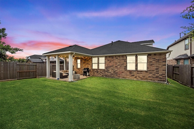rear view of house featuring brick siding, a patio, a yard, and a fenced backyard