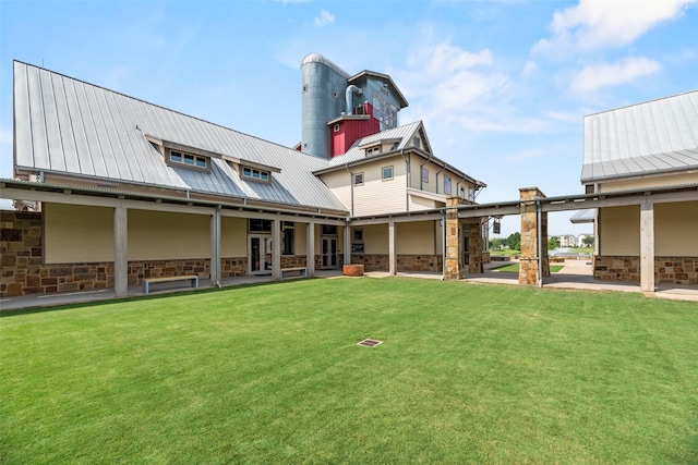 rear view of house featuring a lawn, a patio, metal roof, and stone siding
