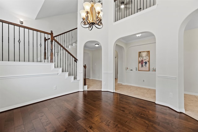 foyer entrance with a notable chandelier, arched walkways, stairs, a towering ceiling, and hardwood / wood-style flooring