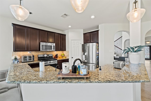 kitchen featuring dark brown cabinetry, appliances with stainless steel finishes, light stone countertops, tasteful backsplash, and visible vents