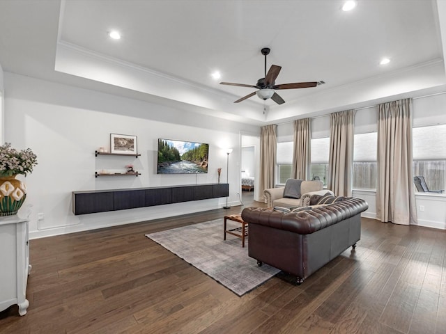 living room with a ceiling fan, a tray ceiling, and dark wood-style floors