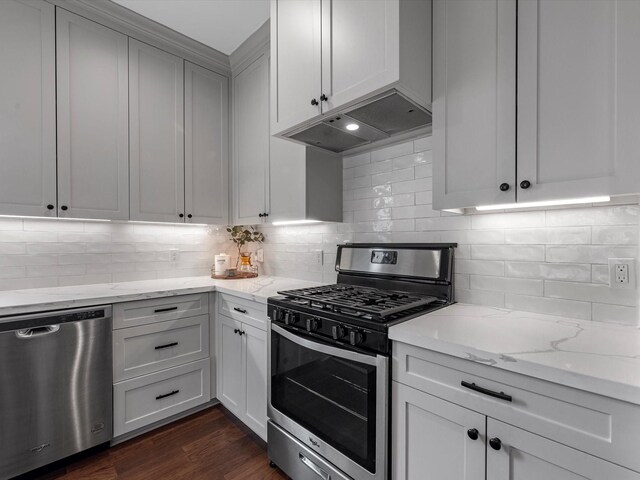 kitchen featuring dark wood-style flooring, appliances with stainless steel finishes, tasteful backsplash, light stone counters, and under cabinet range hood