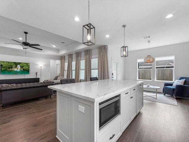 kitchen with dark wood-style flooring, a center island, stainless steel microwave, open floor plan, and visible vents