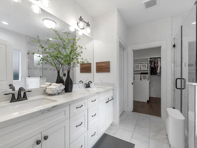 full bathroom with double vanity, a sink, a walk in closet, and a shower stall