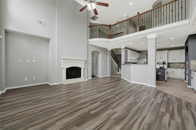 unfurnished living room with ceiling fan, a high ceiling, a fireplace with raised hearth, wood finished floors, and visible vents