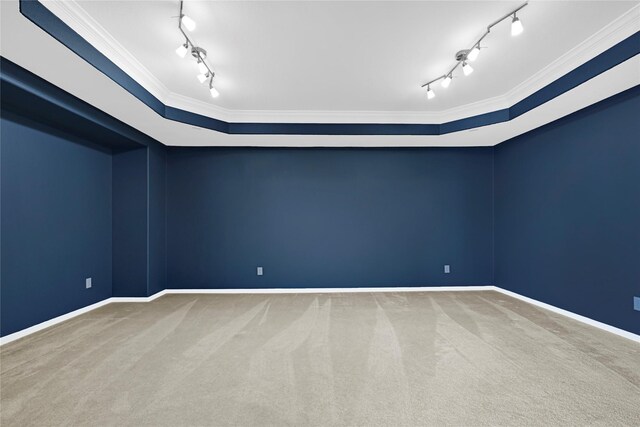 carpeted empty room with crown molding, rail lighting, and baseboards