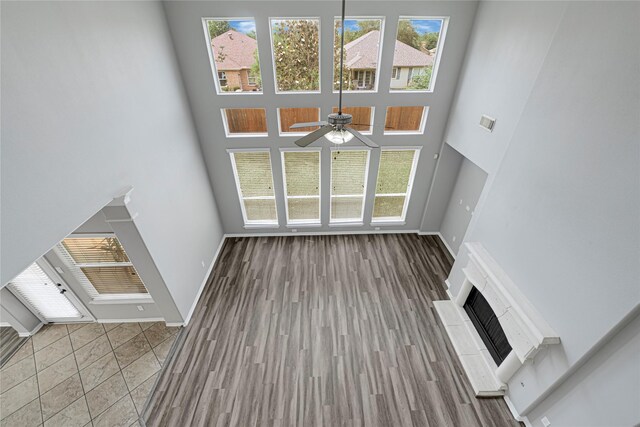unfurnished living room featuring a ceiling fan, baseboards, a fireplace with raised hearth, and a towering ceiling