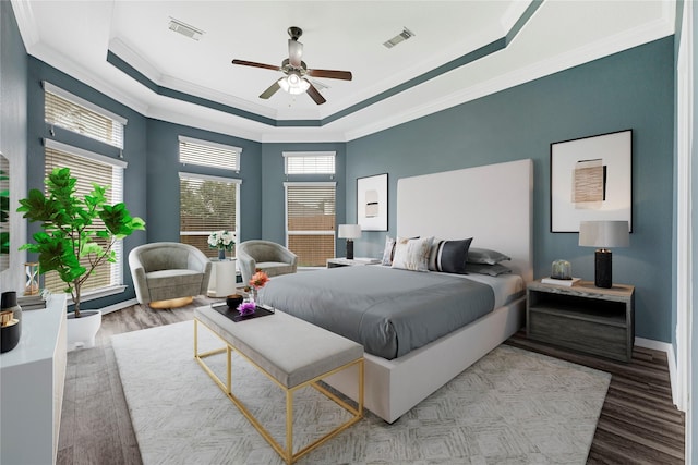 bedroom with crown molding, a tray ceiling, visible vents, and wood finished floors
