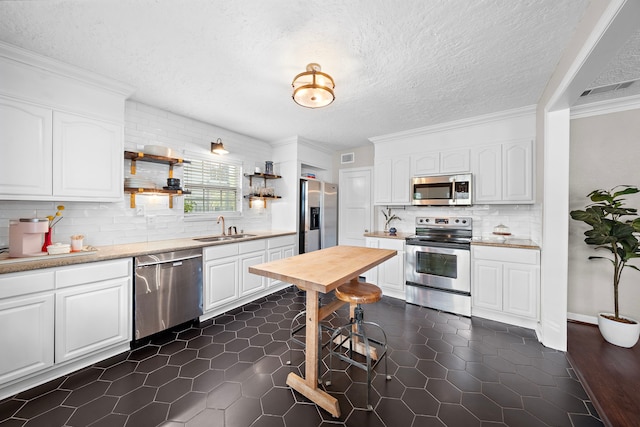kitchen featuring stainless steel appliances, ornamental molding, white cabinetry, and a sink