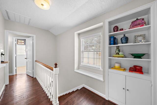 corridor featuring visible vents, lofted ceiling, baseboards, dark wood-style floors, and an upstairs landing