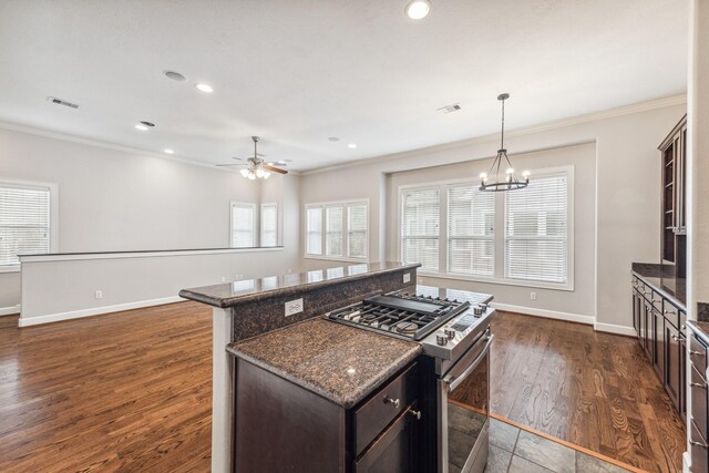 kitchen with crown molding, stainless steel range with gas stovetop, ceiling fan with notable chandelier, baseboards, and visible vents