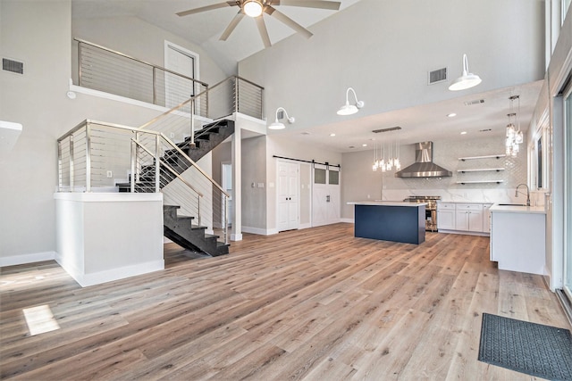 unfurnished living room featuring ceiling fan, a barn door, a sink, high vaulted ceiling, and stairway