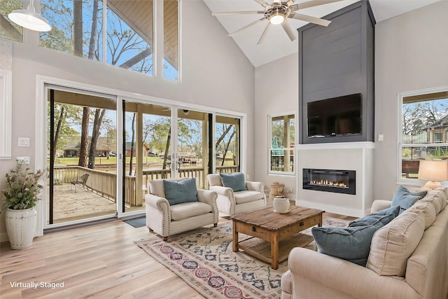 living room with a ceiling fan, light wood finished floors, a glass covered fireplace, and high vaulted ceiling