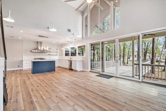 unfurnished living room with high vaulted ceiling, ceiling fan with notable chandelier, light wood finished floors, and a wealth of natural light
