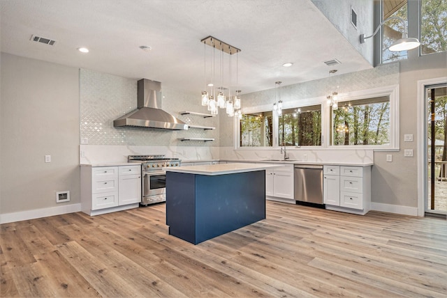 kitchen with visible vents, wall chimney range hood, white cabinetry, a sink, and appliances with stainless steel finishes