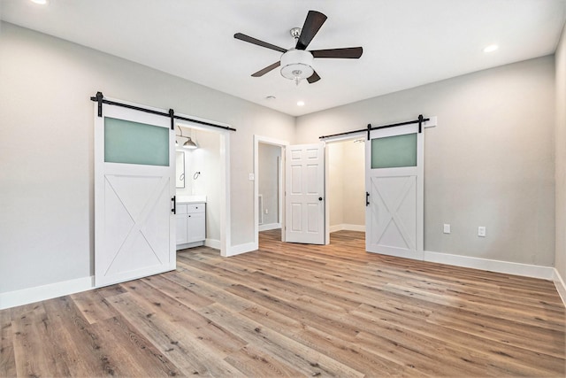 unfurnished bedroom featuring baseboards, light wood-style flooring, recessed lighting, and a barn door
