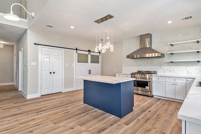 kitchen with a barn door, wall chimney exhaust hood, high end stove, light wood-type flooring, and visible vents
