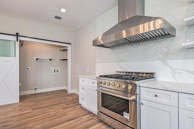 kitchen with wall chimney range hood, decorative backsplash, visible vents, high end stove, and light wood-type flooring