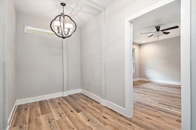 unfurnished dining area featuring baseboards, ceiling fan with notable chandelier, and light wood-type flooring