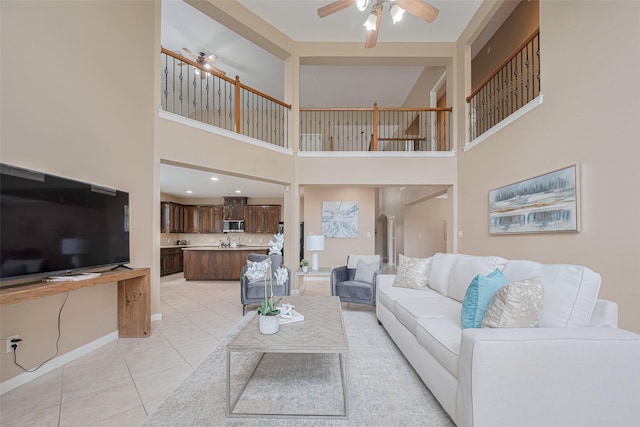 living area featuring light tile patterned floors, baseboards, ceiling fan, and a towering ceiling