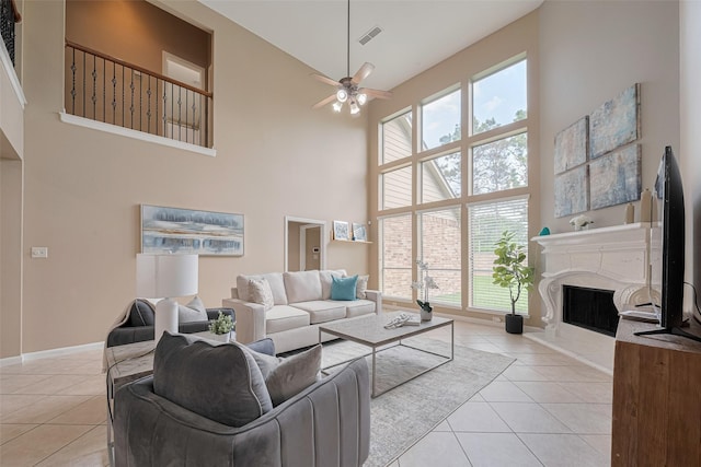 living room with ceiling fan, visible vents, light tile patterned floors, high vaulted ceiling, and a fireplace with raised hearth