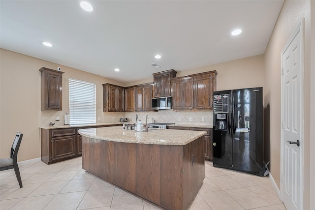 kitchen featuring decorative backsplash, dark brown cabinets, stainless steel microwave, and black fridge