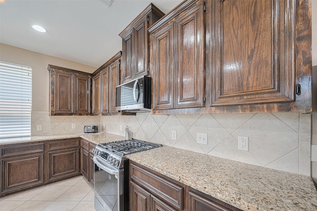 kitchen featuring stainless steel appliances, light stone countertops, dark brown cabinets, and tasteful backsplash