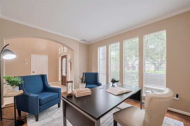 office space featuring crown molding, visible vents, baseboards, arched walkways, and light wood-style flooring
