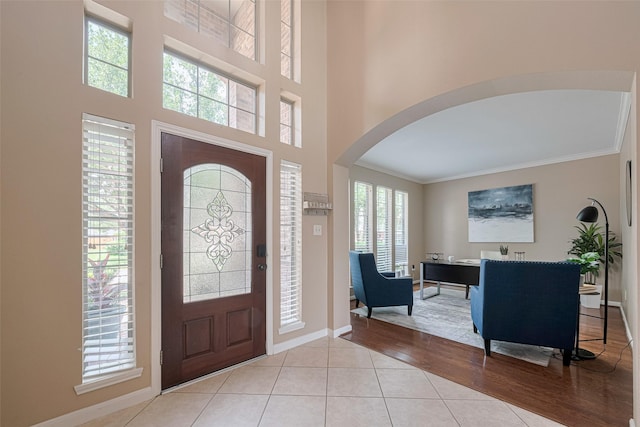 foyer with crown molding, arched walkways, baseboards, and a healthy amount of sunlight