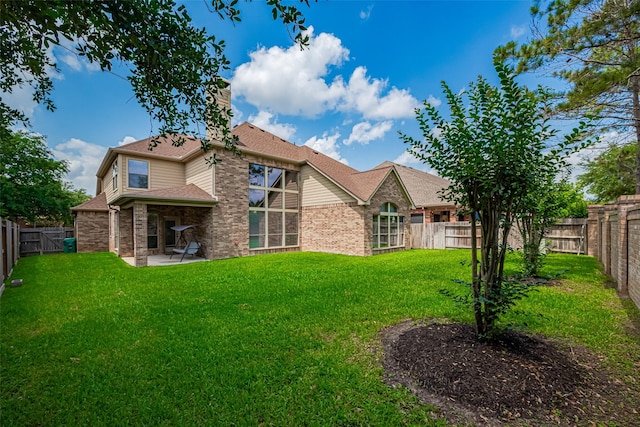 rear view of property featuring roof with shingles, brick siding, a fenced backyard, a patio, and a yard