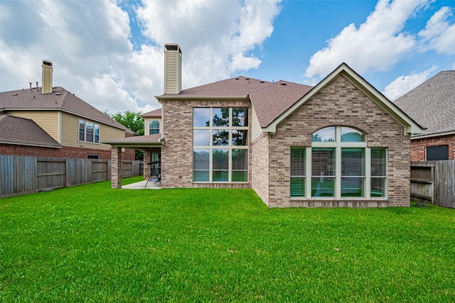 back of house featuring brick siding, a fenced backyard, a yard, a patio, and a shingled roof