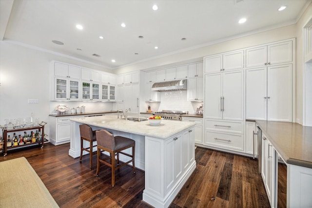 56 Audubon Hollow Ln, Houston, TX 77027 - kitchen with glass insert cabinets, under cabinet range hood, dark wood finished floors, and white cabinetry