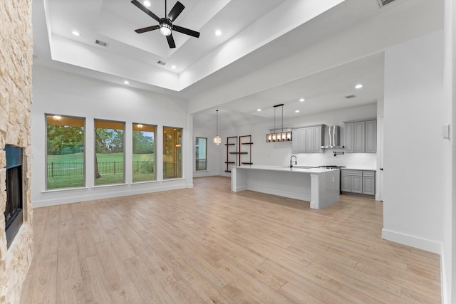 unfurnished living room with a ceiling fan, visible vents, a fireplace, a sink, and light wood-style flooring