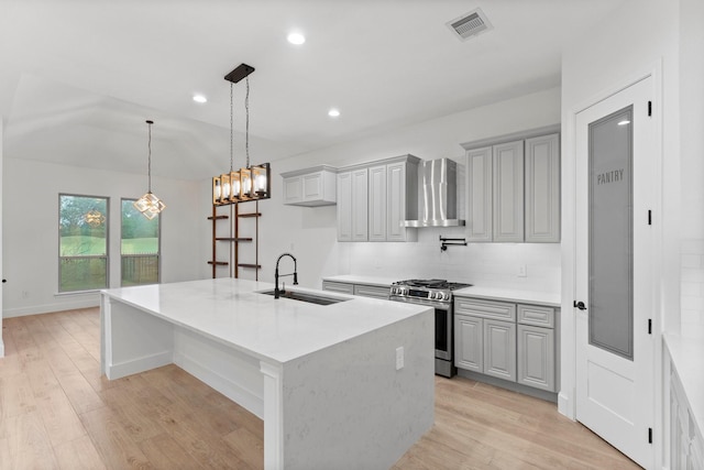 kitchen with visible vents, light wood-style floors, wall chimney range hood, stainless steel gas range, and a sink