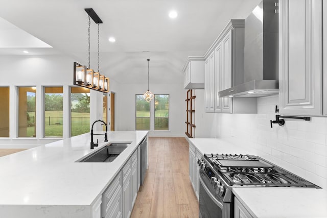 kitchen with a sink, light wood-style floors, stainless steel appliances, recessed lighting, and wall chimney exhaust hood