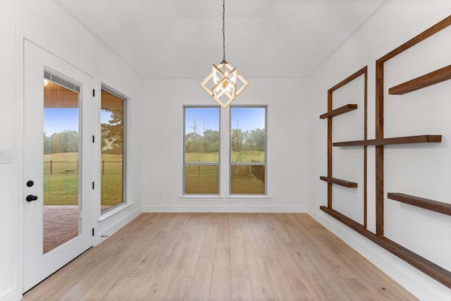 unfurnished dining area with an inviting chandelier, light wood finished floors, and baseboards