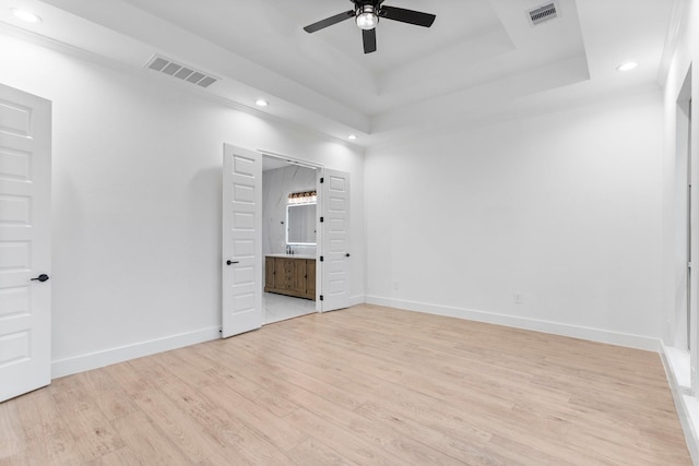 unfurnished bedroom featuring visible vents, recessed lighting, light wood-style flooring, and a raised ceiling