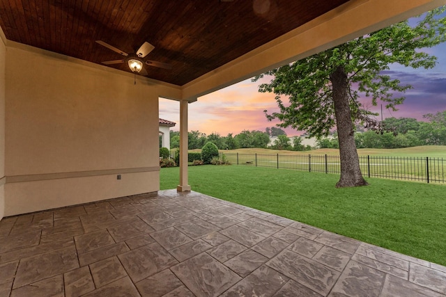 patio terrace at dusk featuring a lawn, a fenced backyard, and ceiling fan