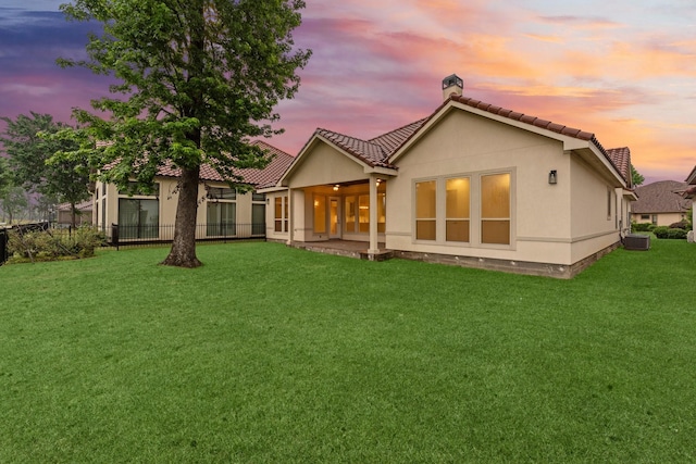 back of property with cooling unit, stucco siding, a chimney, a lawn, and a tile roof
