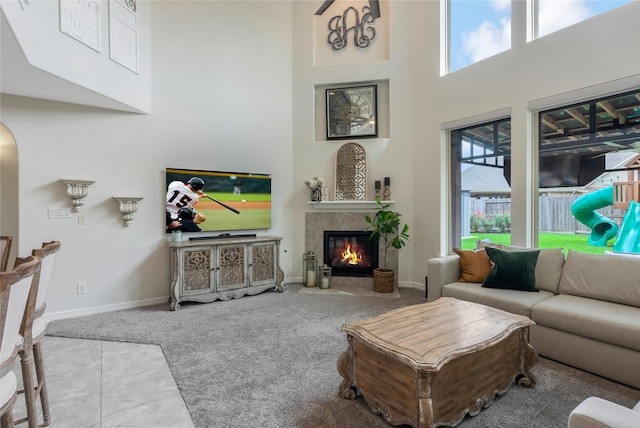 tiled living room featuring carpet flooring, a high ceiling, a fireplace, arched walkways, and baseboards