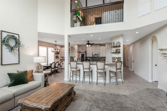 living room featuring recessed lighting, ceiling fan with notable chandelier, and a towering ceiling