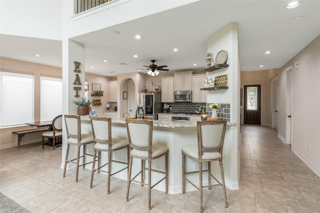 kitchen featuring a kitchen breakfast bar, backsplash, light stone countertops, stainless steel microwave, and recessed lighting